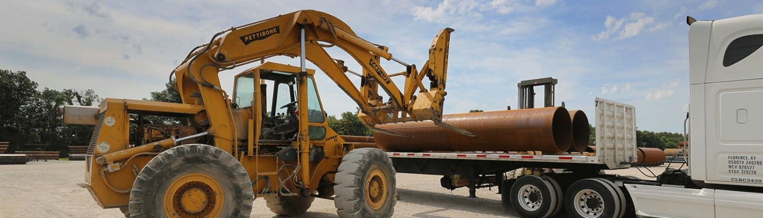 Front loader tractor loading large pipes on a truck