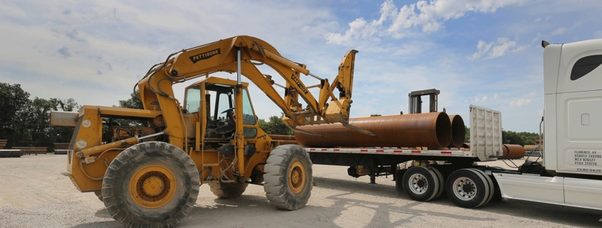 Front loader tractor loading large pipes on a truck