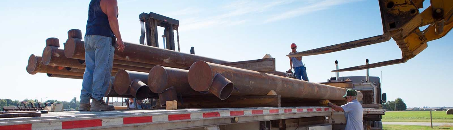 workers unloading large pipes from truck